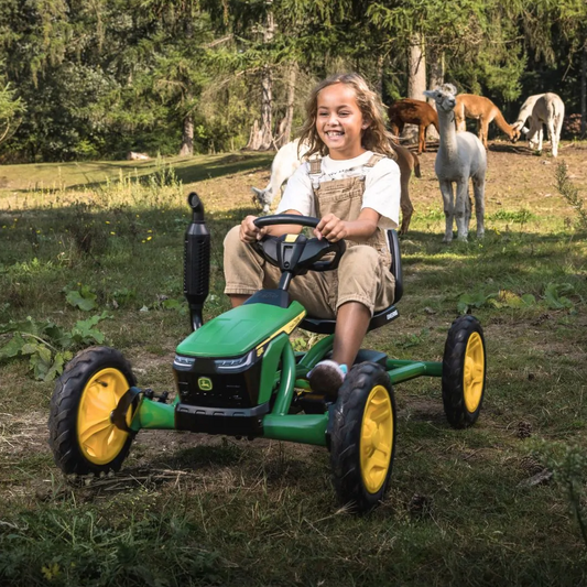 Young girl riding a BERG Buzzy John Deere kids pedal go-kart in a grassy field