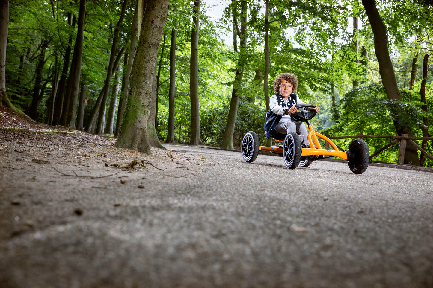 Child riding BERG Buddy B-Orange pedal go-kart outdoors