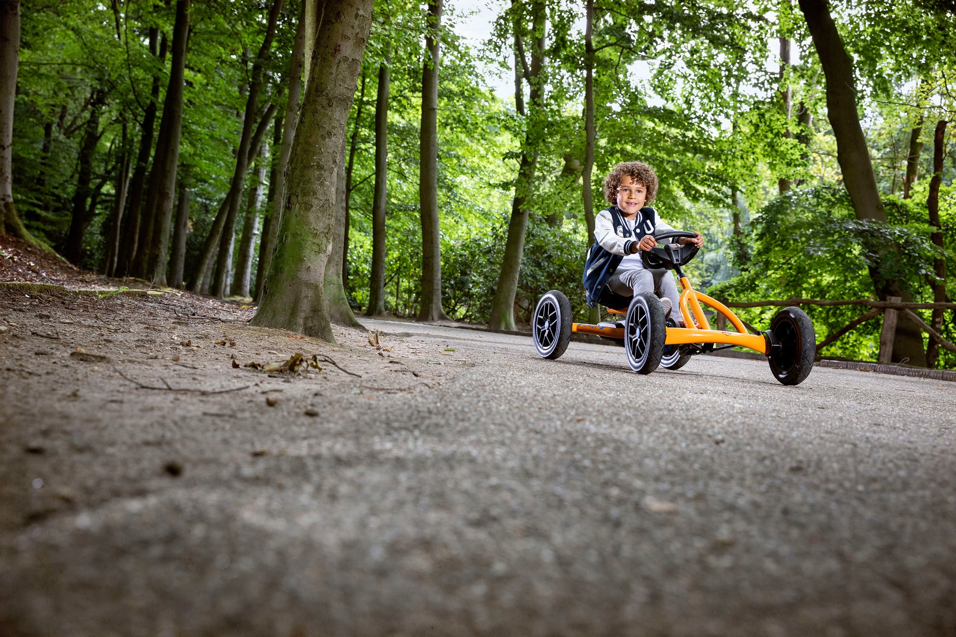 Child riding BERG Buddy B-Orange pedal go-kart outdoors