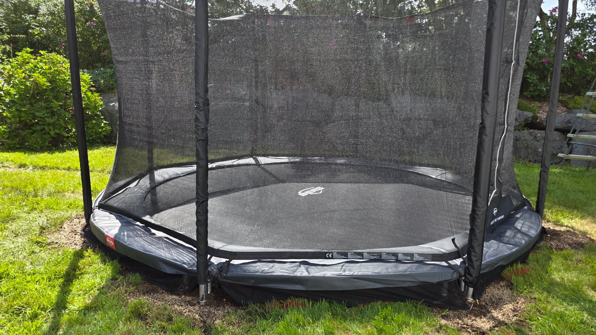 Hooking the springs to the jump mat and placing the green safety padding on a finished Berg inground trampoline.