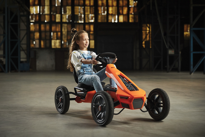 Child riding BERG Rally Orange pedal go-kart outdoors