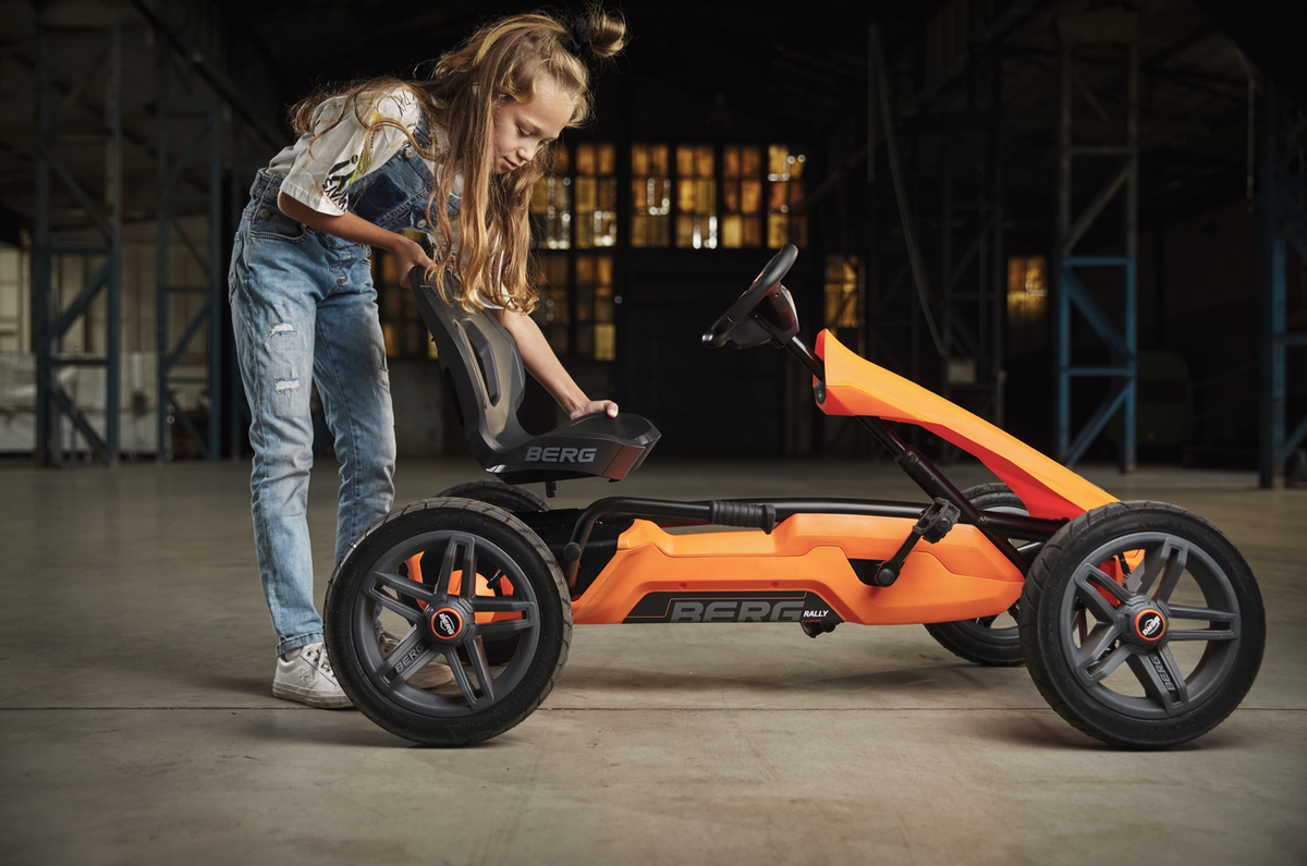 Child riding BERG Rally Orange pedal go-kart outdoors