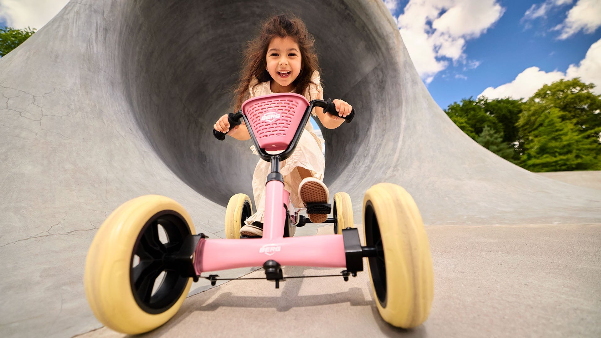 Happy kids using the BERG Buzzy Pink ride-on pedal kart outdoors