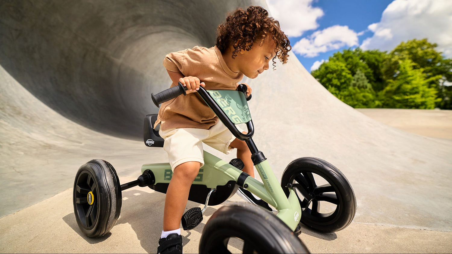 Young child riding the BERG Buzzy Green go-kart in a sunny park