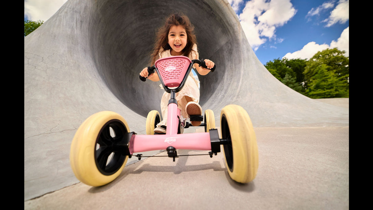 Young girl riding the BERG Buzzy Pink go-kart in a sunny park